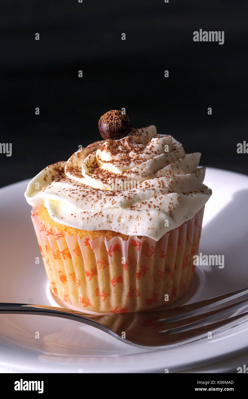 Cupcake Tiramisu sur une assiette avec une fourchette. Sur la table. Chocolats surmontée. ; Angel food cupcake et crème de mascarpone. Fond sombre. Dans la coupe. Banque D'Images