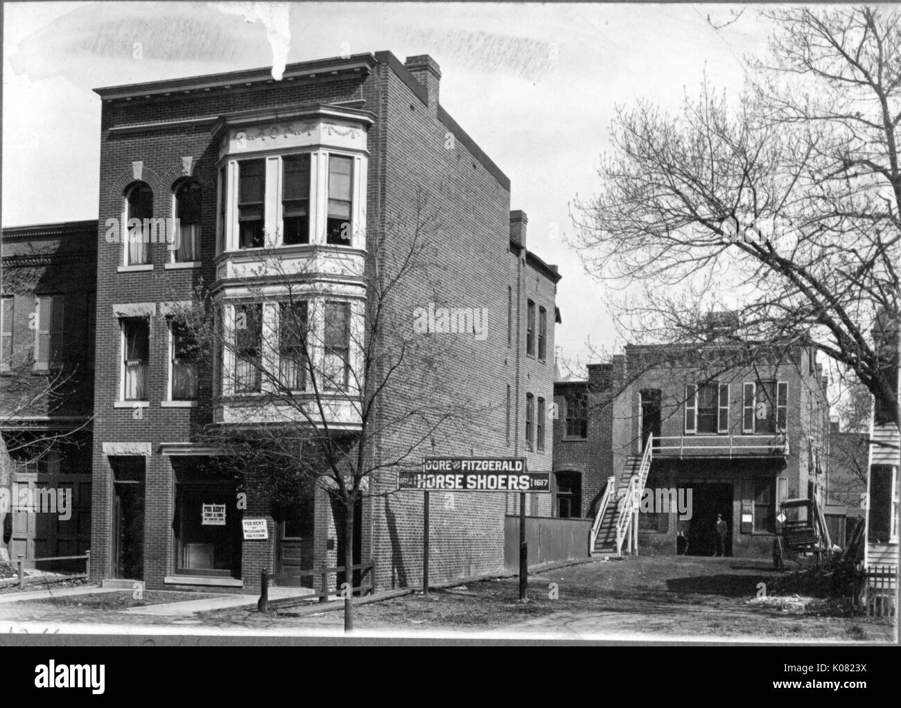 Un écriteau 'Dore et Fitzgerald l'Shoers' est situé en face d'un bâtiment avec l'escalier qui mène au deuxième étage, une véranda, un garage-comme l'ouverture, et un chariot élévateur en face d'elle, et le signe est à côté d'un bâtiment avec Rick b 'A LOUER' signes et de grandes fenêtres en baie, à Baltimore, Maryland, 1910. Cette image est tirée d'une série sur la construction et la vente de maisons dans le quartier Roland Park/Guilford de Baltimore, a streetcar suburb et l'une des premières communautés planifiées aux États-Unis. Banque D'Images