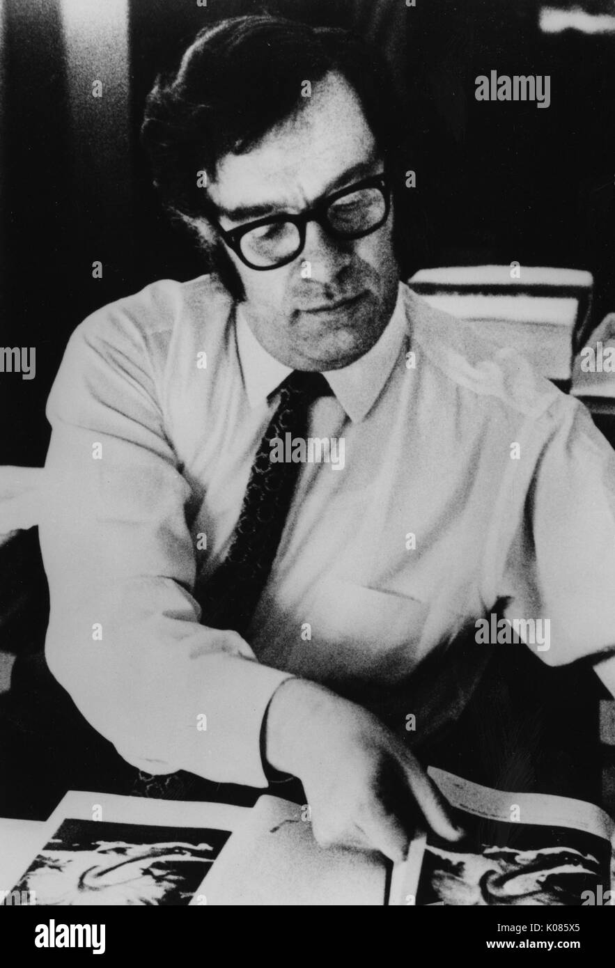 Portrait de demi-longueur auteur Isaac Asimov, portant une chemise blanche, assis sur une table, feuilleter les pages d'un livre, portant des lunettes et une cravate à motifs, avec une expression du visage grave, 1970. Banque D'Images