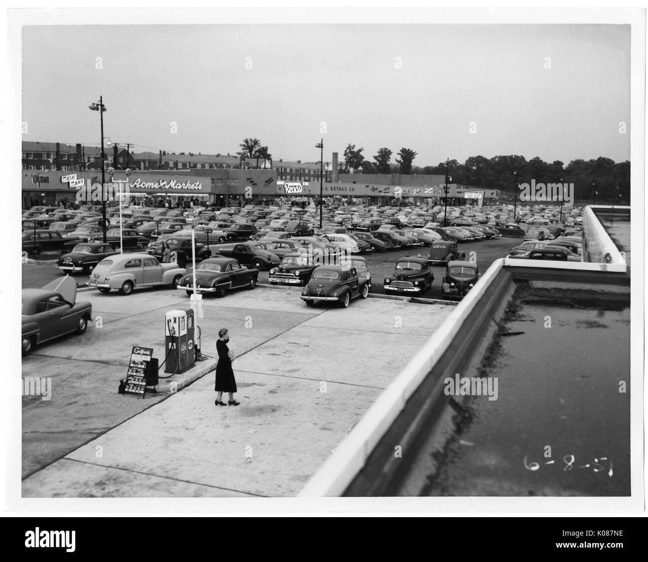 Vue d'un panier-parking et centre commercial du toit d'une station d'essence, une femme se tient debout à l'extérieur de la station service, à l'arrière-plan derrière le centre commercial sont en rangée et d'arbres, Baltimore, Maryland, 1951. Banque D'Images