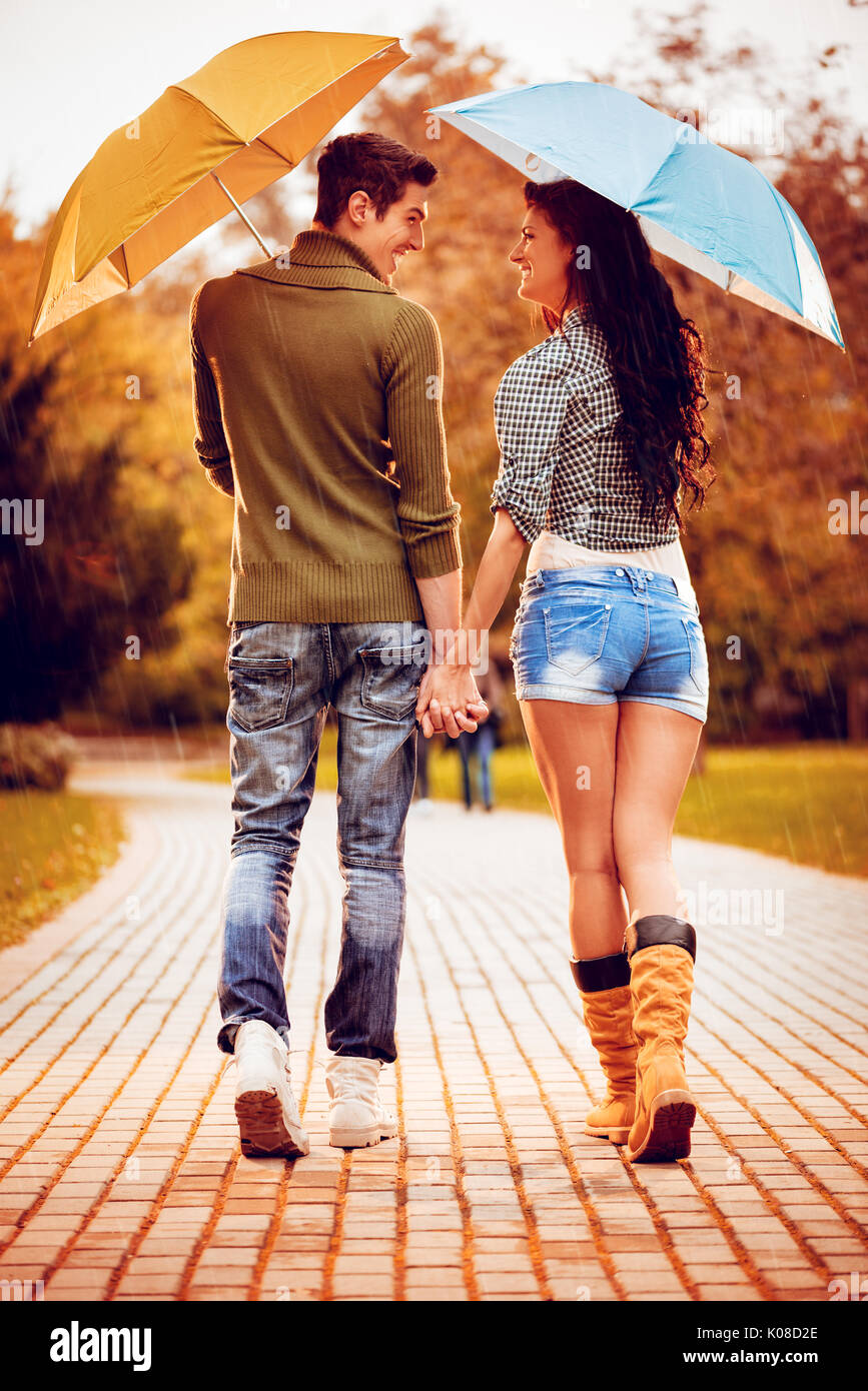 Quel beau couple magnifique avec parasols bénéficiant en marchant sous la pluie à travers le parc en automne couleurs. vue arrière. Banque D'Images