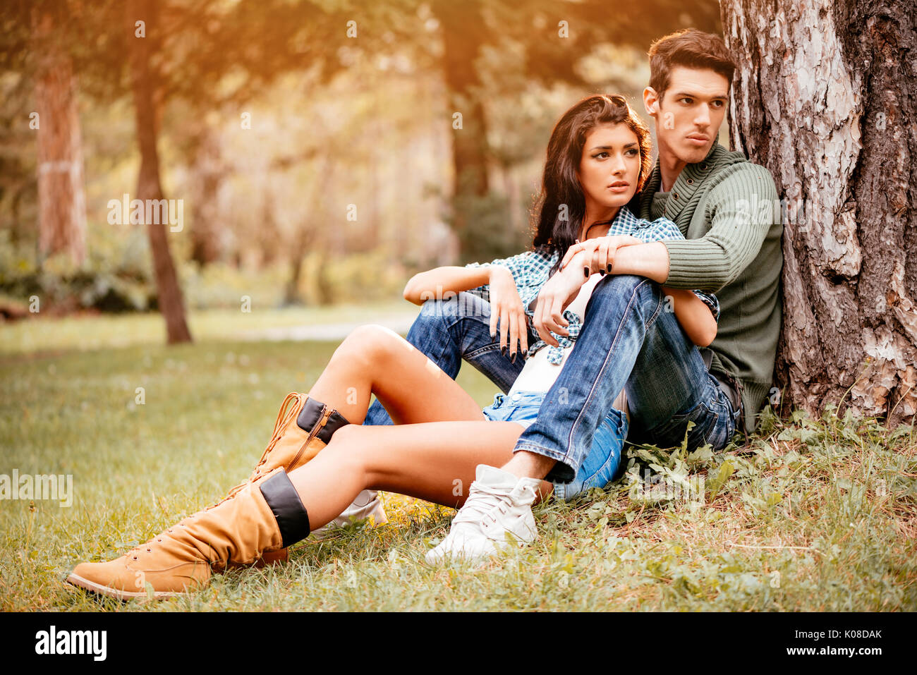 Belle lovely couple assis sur l'herbe à côté de l'arbre et bénéficiant à sunny park en couleurs de l'automne. Banque D'Images