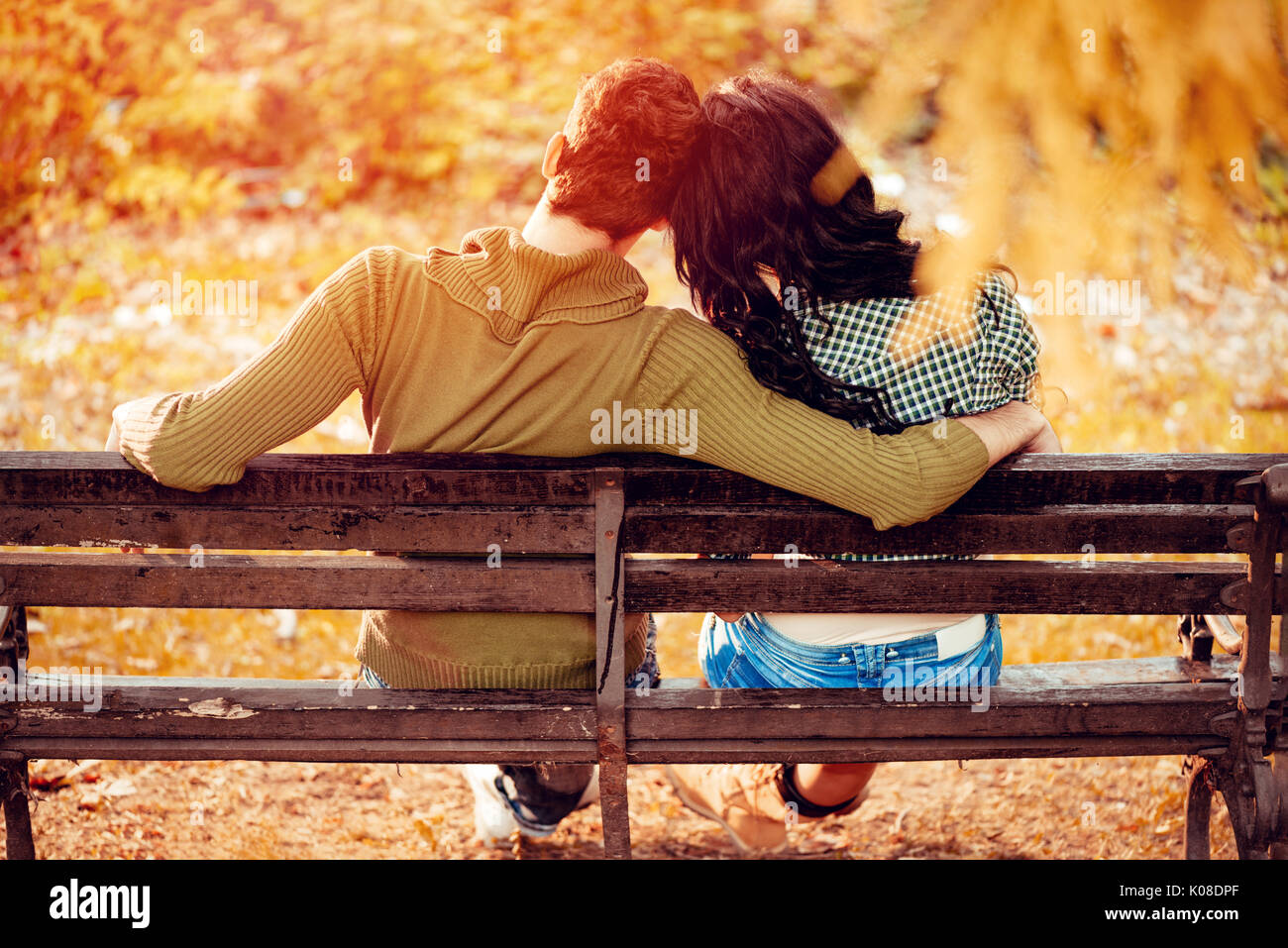 Belle lovely couple assis sur le banc et profiter à sunny park en couleurs de l'automne. vue arrière. Banque D'Images