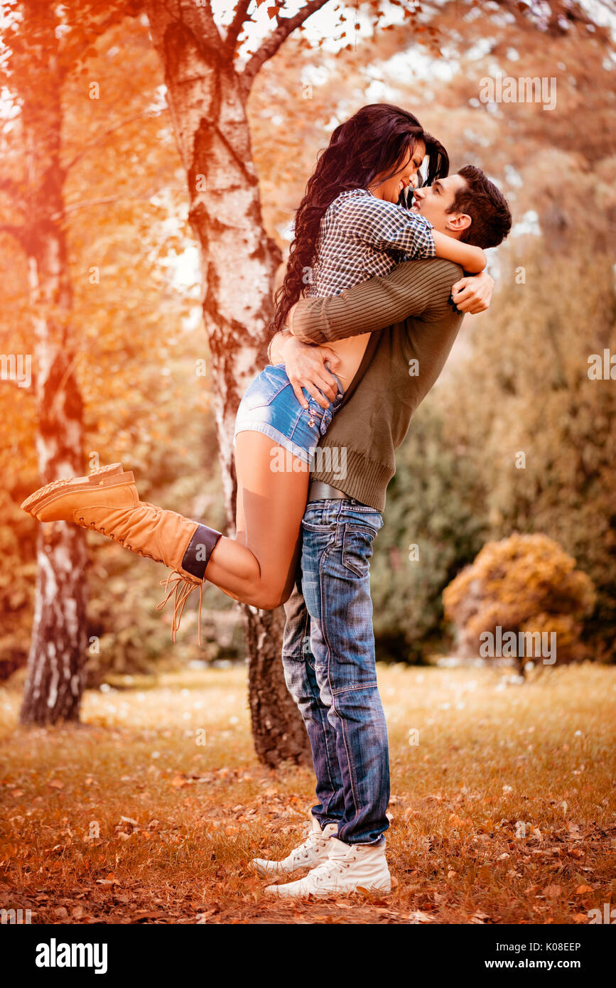 Belle lovely couple enjoying in sunny park en couleurs de l'automne. guy holding petite amie en hauteur dans une étreinte passionnée. Banque D'Images