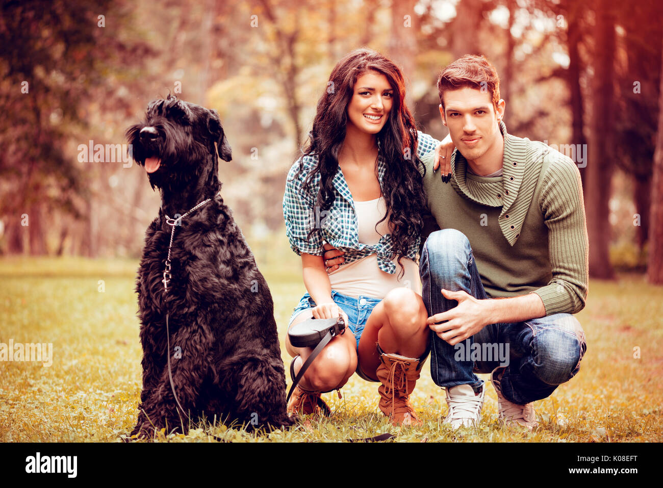 Belle quel beau couple avec un chien, un Schnauzer Géant Noir, bénéficiant dans le parc en couleurs de l'automne. looking at camera. Banque D'Images