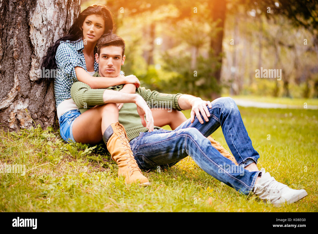 Belle lovely couple assis sur l'herbe à côté de l'arbre et bénéficiant à sunny park en couleurs de l'automne. Banque D'Images