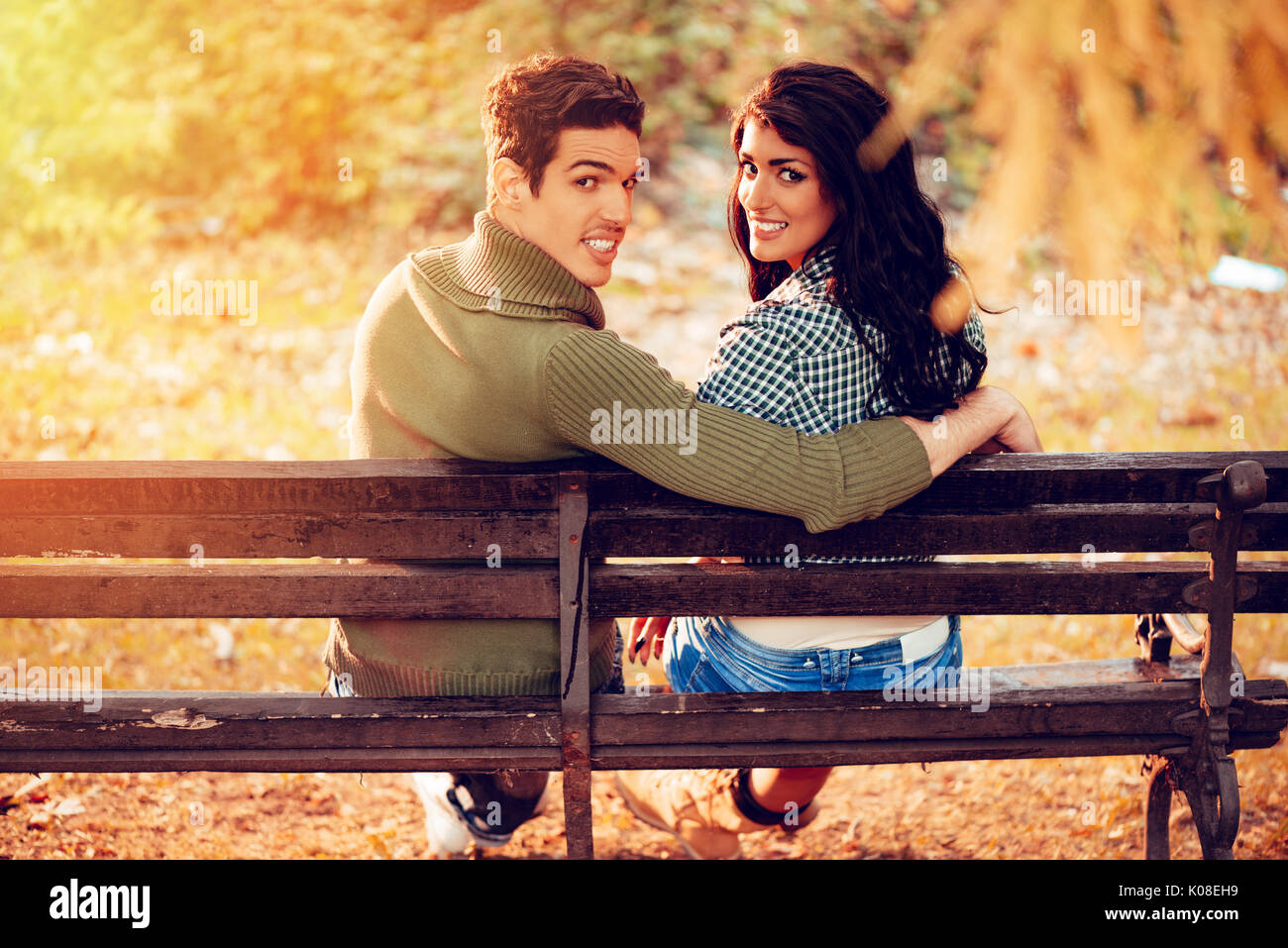 Belle lovely couple assis sur le banc et profiter à sunny park en couleurs de l'automne. looking at camera. vue arrière. Banque D'Images