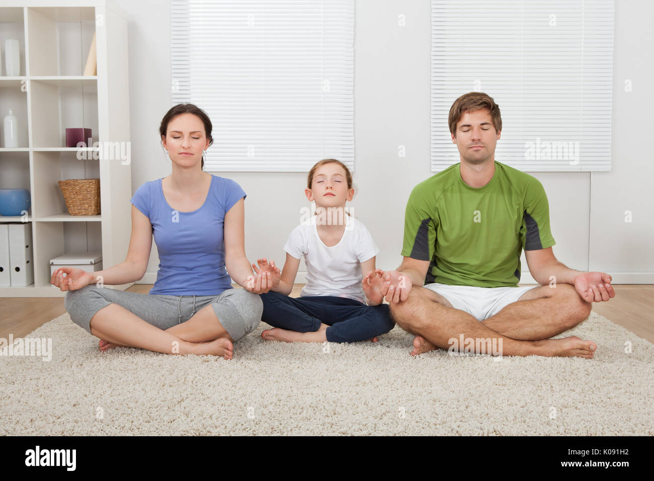 Toute la longueur de la famille fit les yeux fermés la pratique du yoga sur un tapis à la maison Banque D'Images