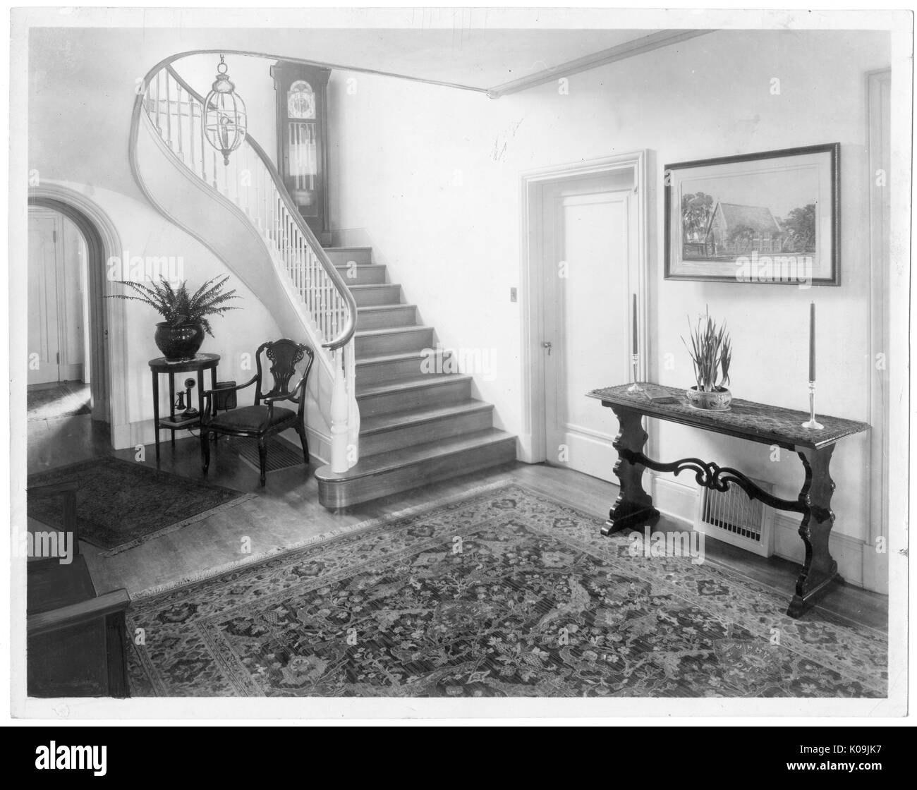 Le hall d'un Guilford House, il y a un tapis à l'avant-plan et un escalier en bois en arrière-plan, il y a quelques morceaux de meubles dans la chambre comme une table de bougies et d'une chaise et d'une petite table avec une plante, Baltimore, Maryland, 1910. Cette image est tirée d'une série sur la construction et la vente de maisons dans le quartier Roland Park/Guilford de Baltimore, a streetcar suburb et l'une des premières communautés planifiées aux États-Unis. Le quartier a été isolé, et est considéré comme l'un des premiers exemples de l'application de la ségrégation raciale à travers l'utilisation des r Banque D'Images