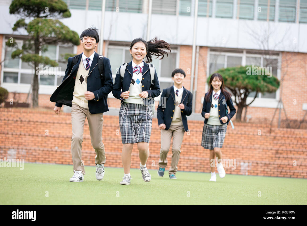 Quatre étudiants de l'école sourire courir contre l'école Banque D'Images