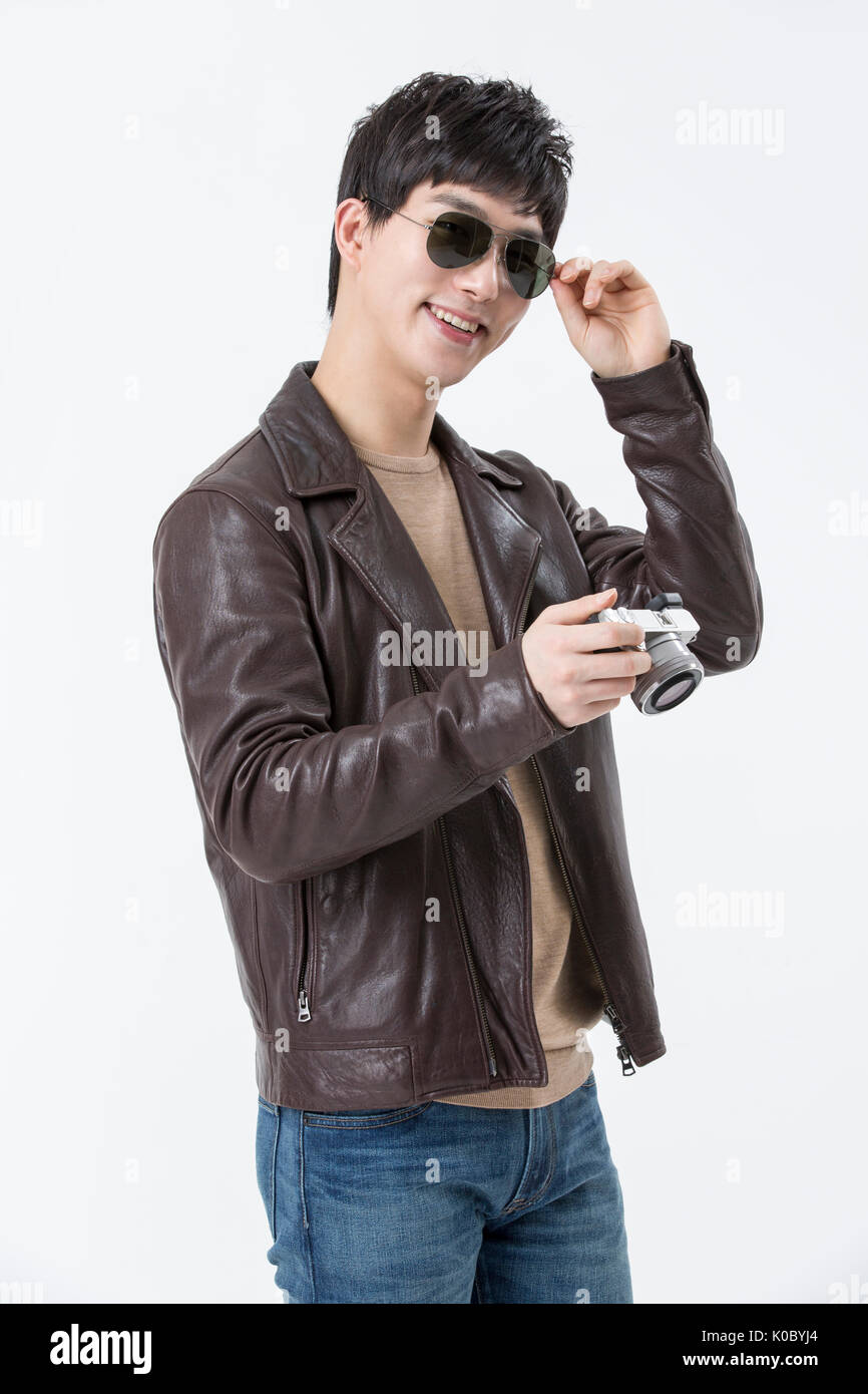 Jeune homme souriant avec des lunettes de soleil et veste de cuir holding a camera Banque D'Images