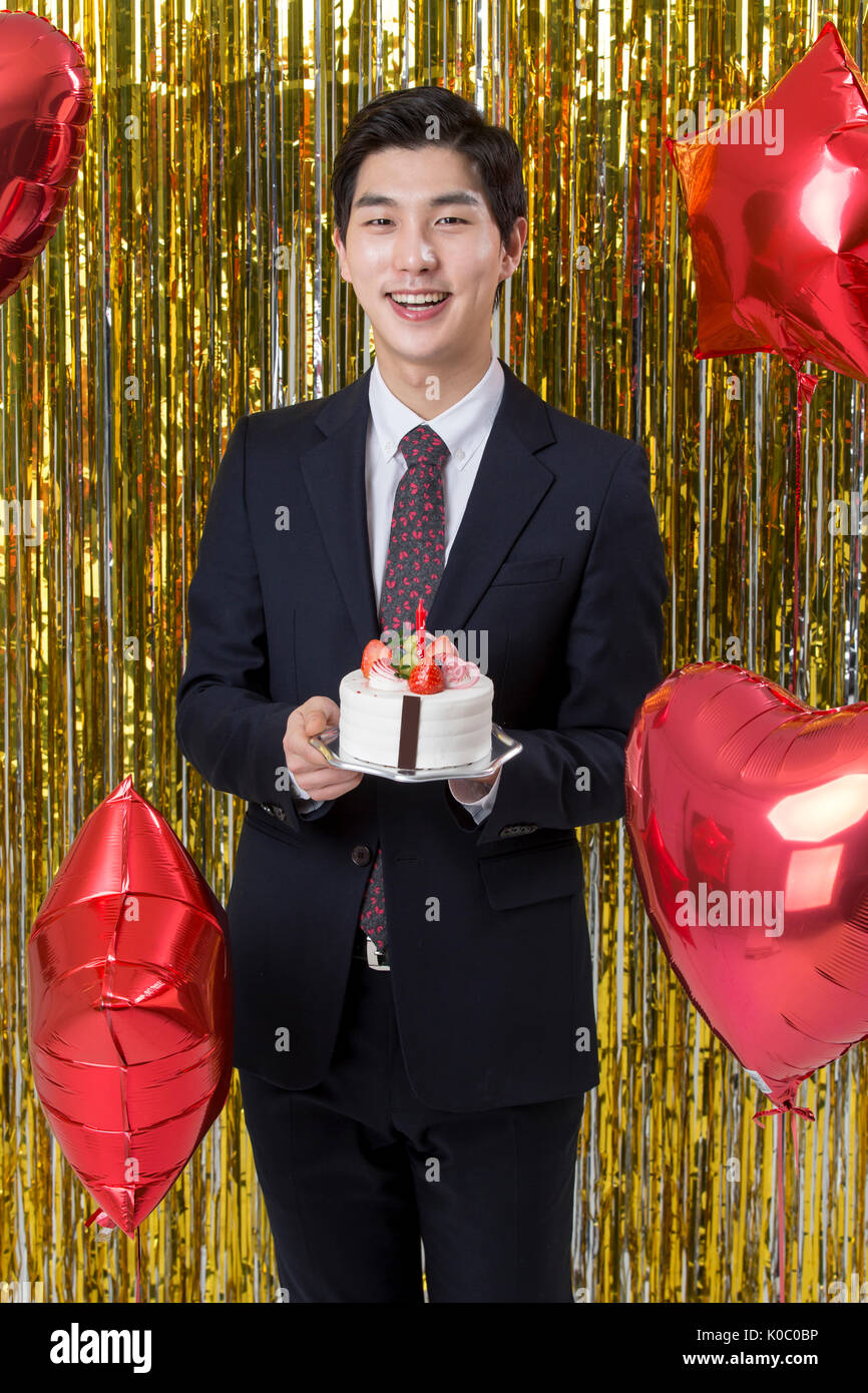 Smiling Young man in suit holding a cake at party Banque D'Images