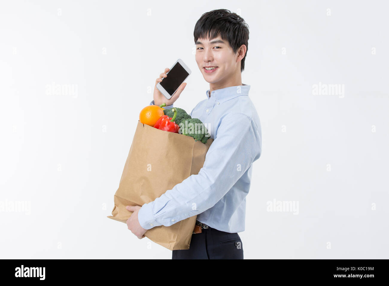 Side view of young smiling man avec panier et smartphone Banque D'Images