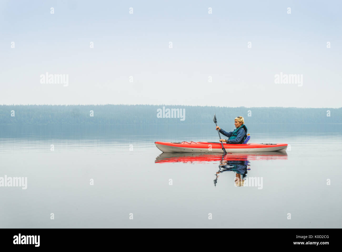 Femme heureuse de pagayer de red kayak sur lac calme, Alberta, Canada Banque D'Images