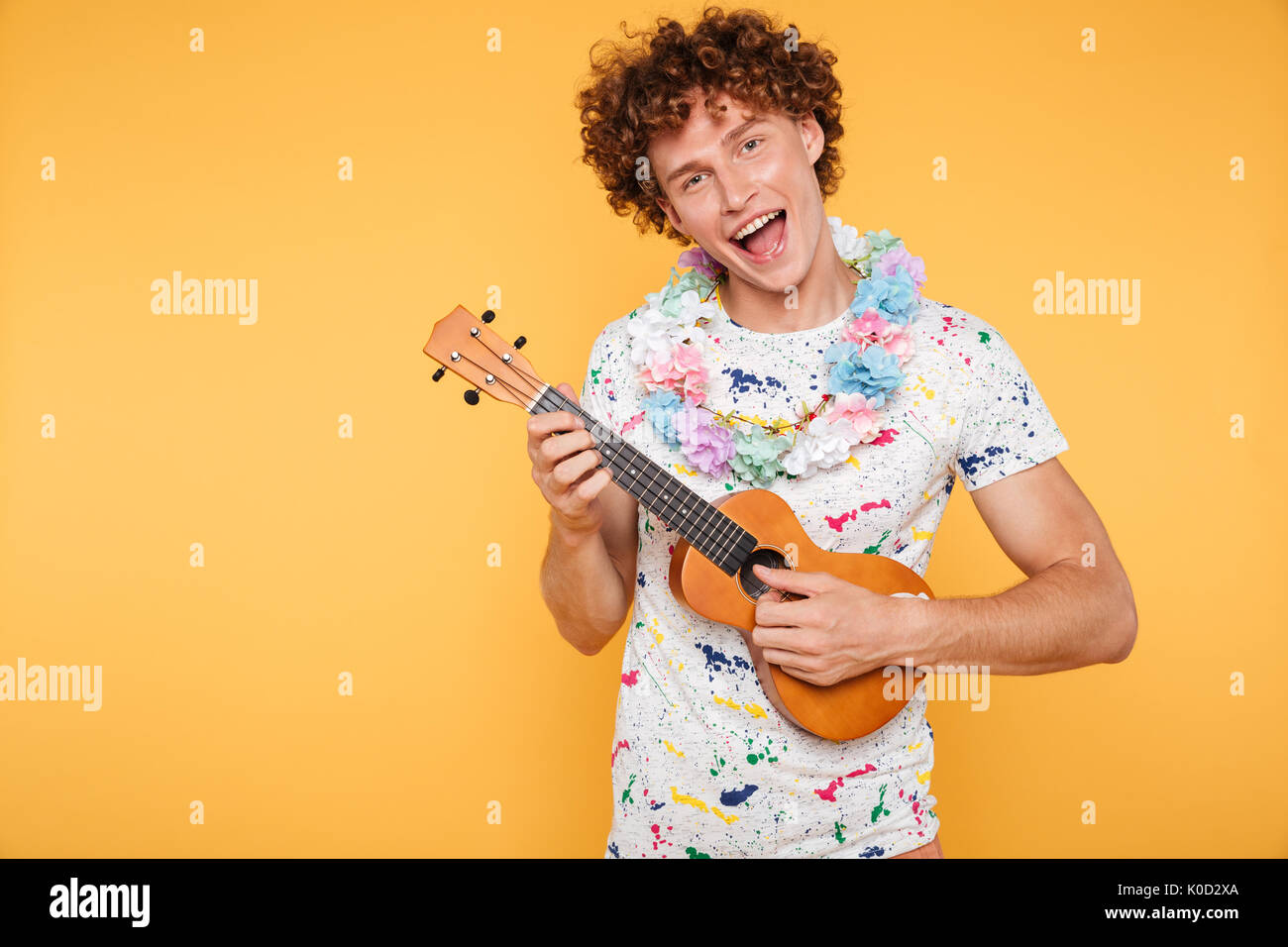 Beau jeune homme dans des vêtements d'été à l'ukulele et de chant sur fond jaune isolé Banque D'Images