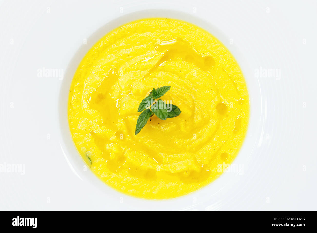 Potage de citrouille servi dans une assiette blanche, décorée de feuilles de menthe Banque D'Images