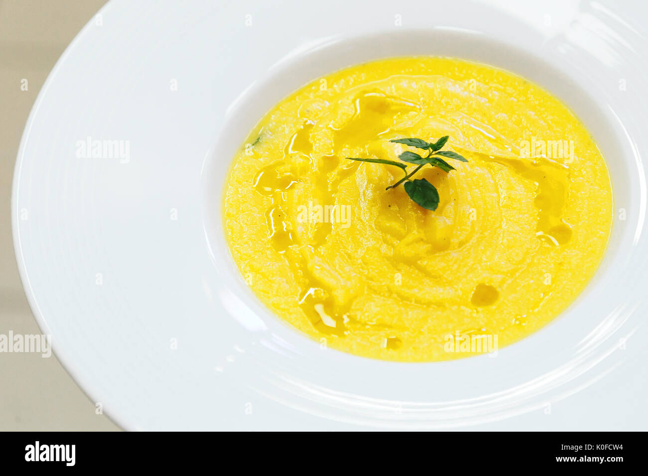 Potage de citrouille servi dans une assiette blanche, décorée de feuilles de menthe Banque D'Images