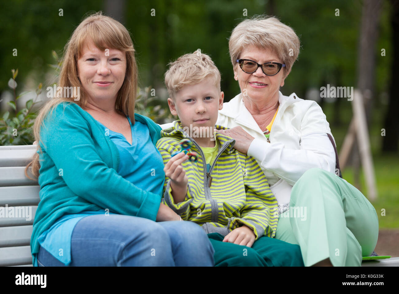 Portrait de famille avec la mère, jeune fils avec spinner et senior grand-mère sur un banc de parc en été Banque D'Images