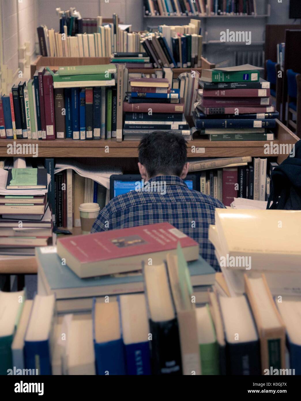 Un étudiant diplômé est assis à son poste de travail sur son ordinateur portable, entouré de piles de livres, dans la bibliothèque Milton S. Eisenhower sur le campus Homewood de l'Université Johns Hopkins à Baltimore, Maryland, 2015. Avec la permission d'Eric Chen. Banque D'Images