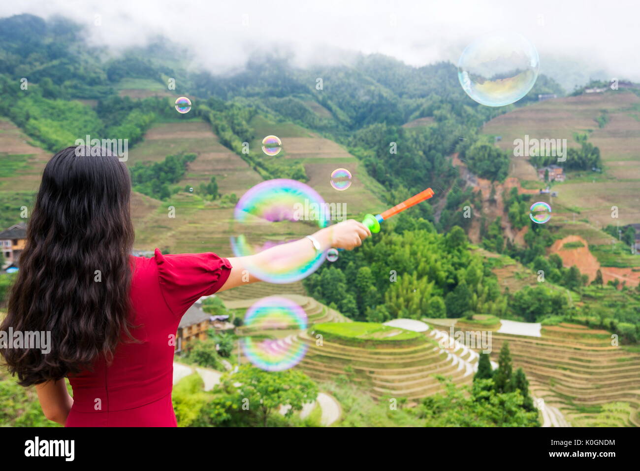 Girl faisant des bulles de savon en vue terrasse de riz portant robe rouge Banque D'Images Girl faisant des bulles de savon en vue terrasse de riz portant robe rouge Banque D'Images