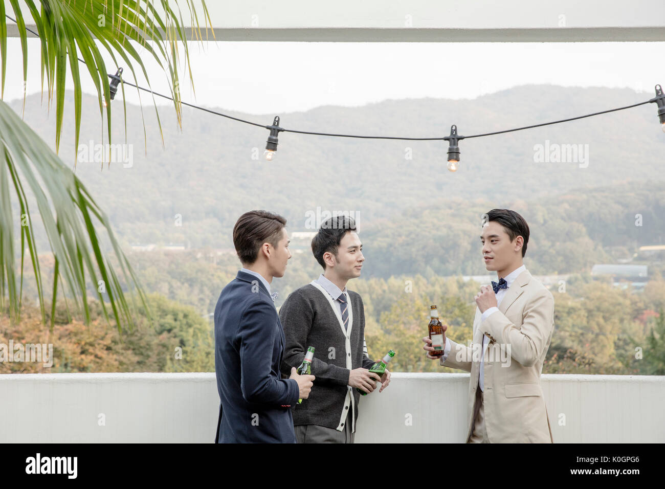 Trois jeunes hommes souriants avec des bouteilles de bière sur le toit à des entretiens Banque D'Images