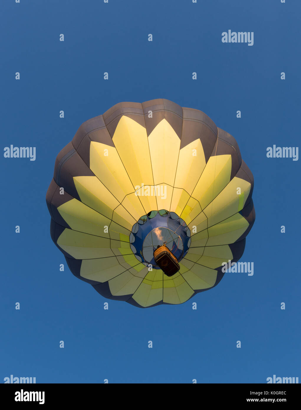 Un jaune et noir en vol en montgolfière. La flamme est vu au-dessus du panier pour transporter des passagers. Le ciel bleu profond est dégagé. Banque D'Images