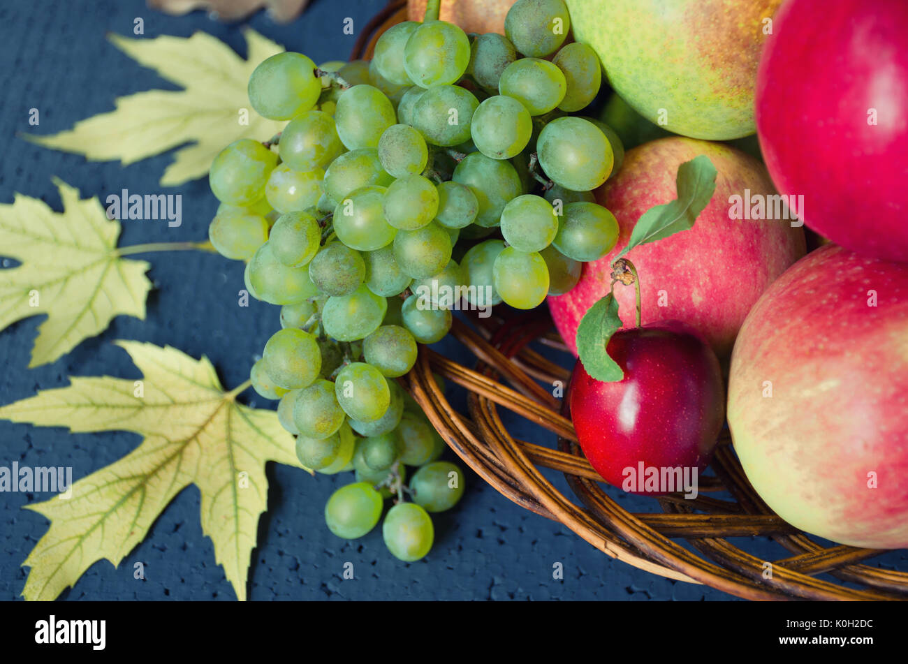 Récolte de fruits mûrs - pommes, raisins, prunes, les poires dans une grande plaque de bois sur un fond noir, décoré avec des feuilles d'érable de l'automne. La récolte d'hiver Banque D'Images