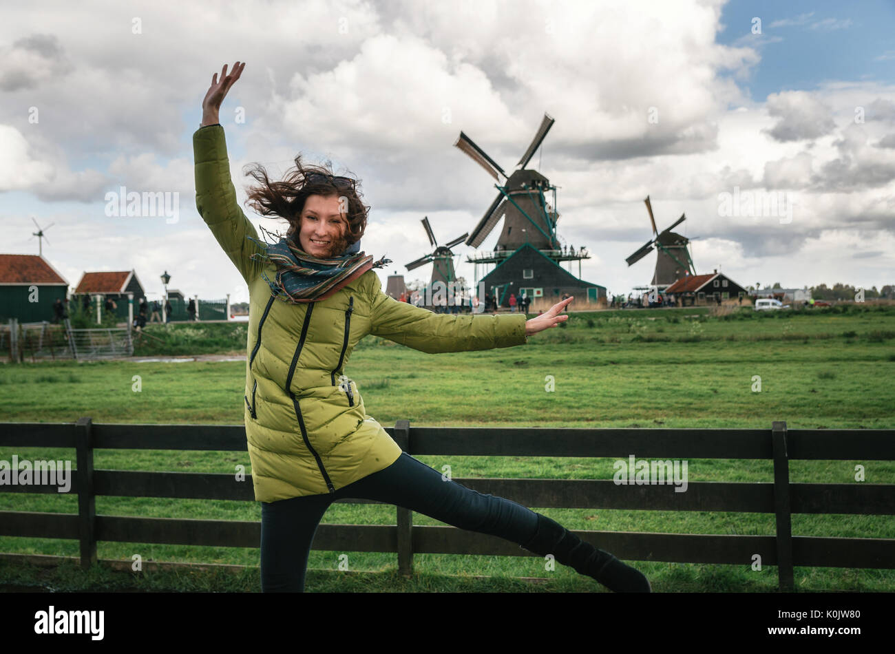 Jeune femme souffle le vent en face d'authentiques moulins Zaandam à Zaanstad village sur la rivière Zaan. Monument de Pays-bas. Banque D'Images