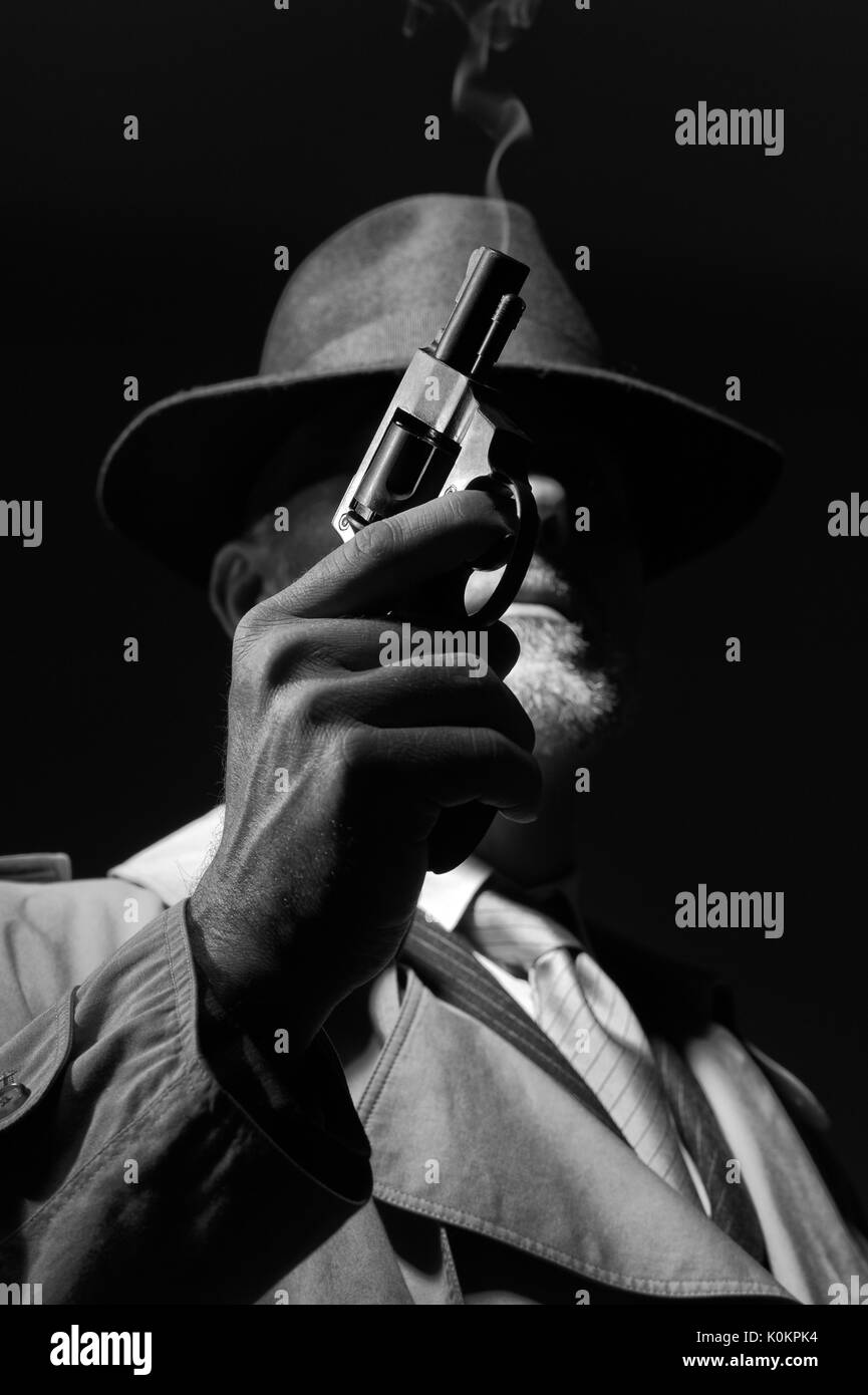 Style années 50 detective posant dans l'obscurité, il est tient une arme et portant un chapeau fedora, personnage de film noir Banque D'Images