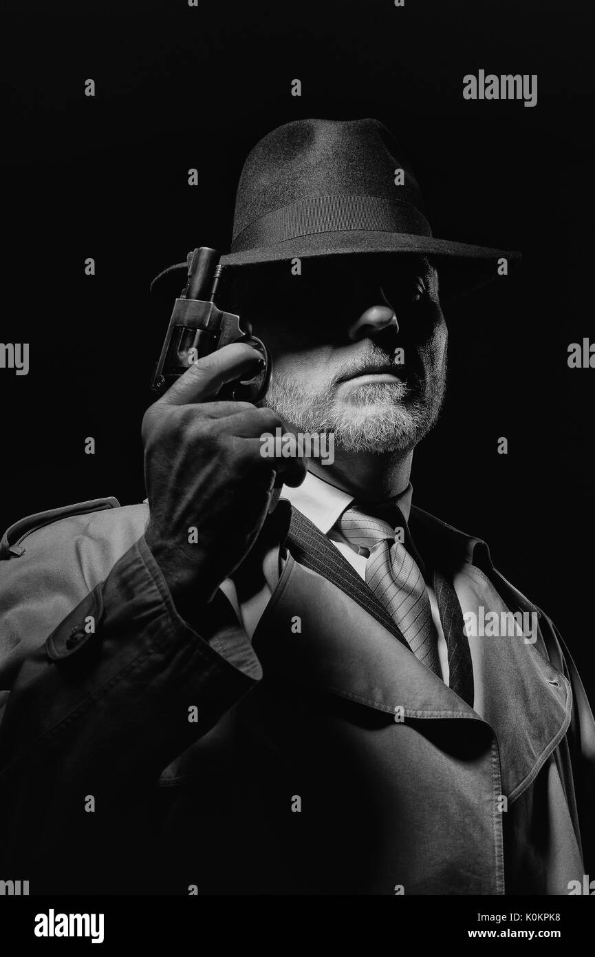 Detective tenant un pistolet dans le noir, il est vêtu d'un chapeau fedora et un trench coat, 1950 personnage film noir Banque D'Images