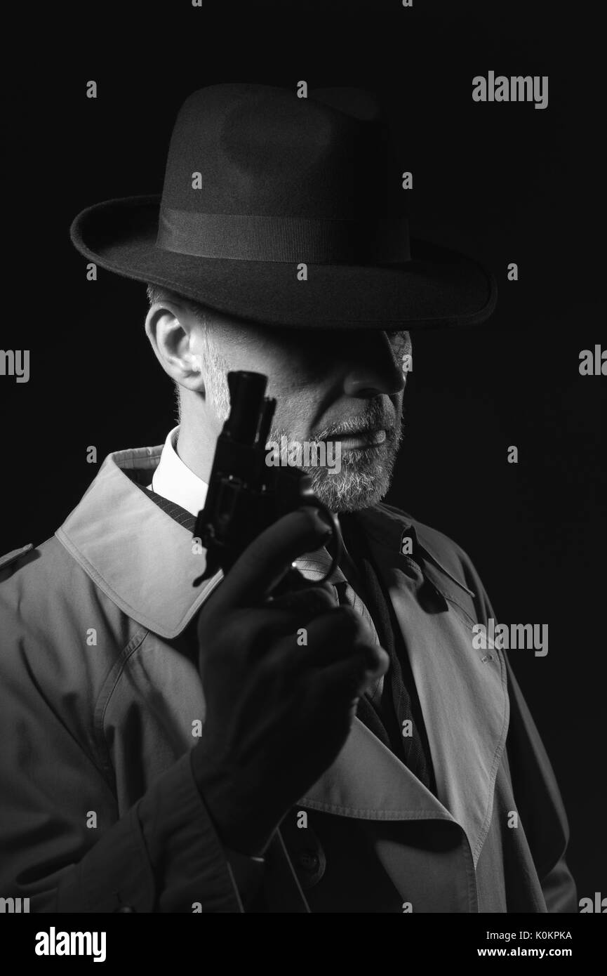 Detective tenant un pistolet, il porte un chapeau fedora et un trench coat, 1950 personnage de film noir Banque D'Images