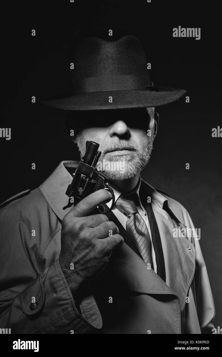 Detective tenant un pistolet dans le noir, il est vêtu d'un chapeau fedora et un trench coat, 1950 personnage film noir Banque D'Images