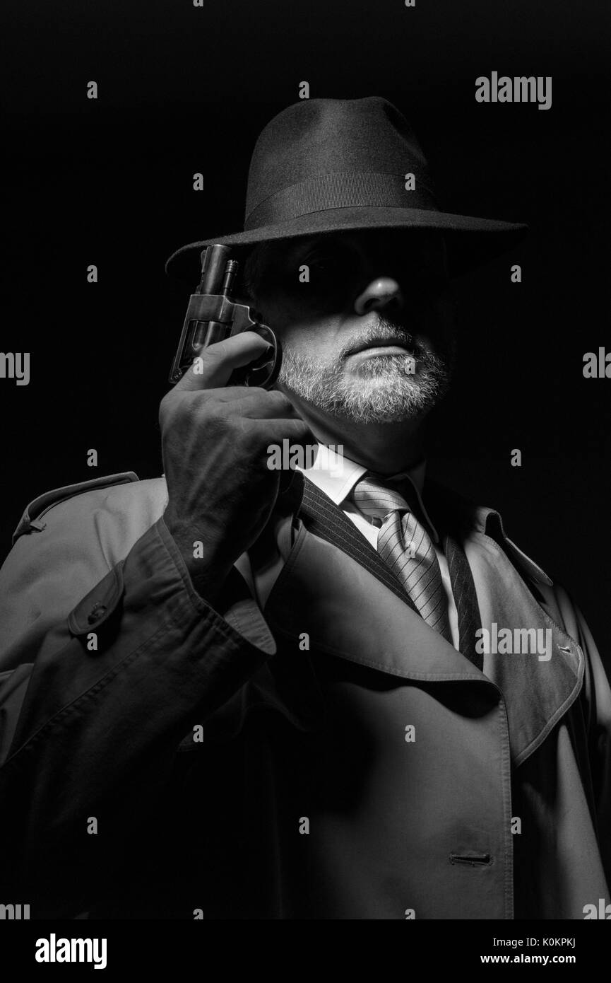 Detective tenant un pistolet dans le noir, il est vêtu d'un chapeau fedora et un trench coat, 1950 personnage film noir Banque D'Images