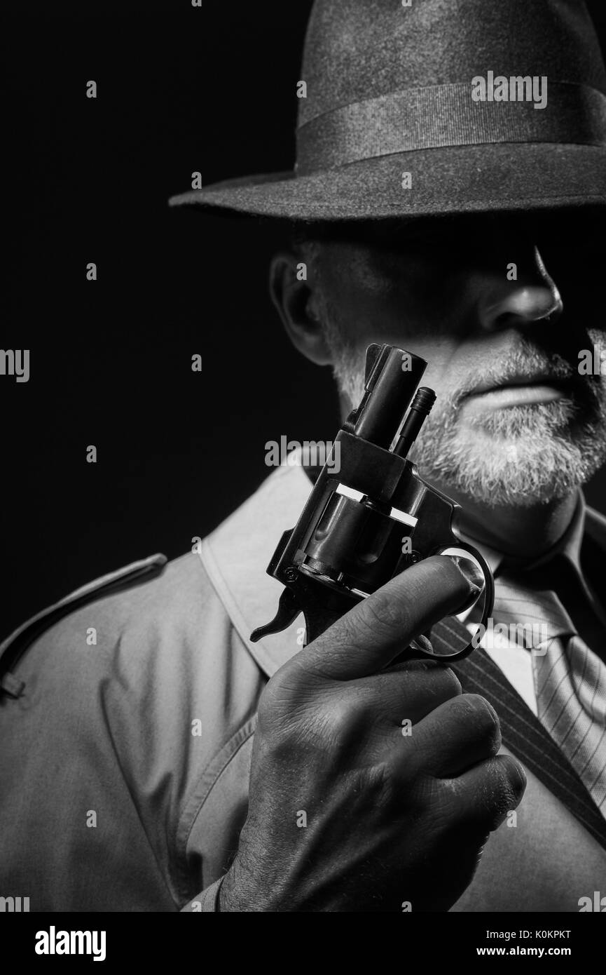 Style années 50 detective posant dans l'obscurité, il est tient une arme et portant un chapeau fedora, personnage de film noir Banque D'Images