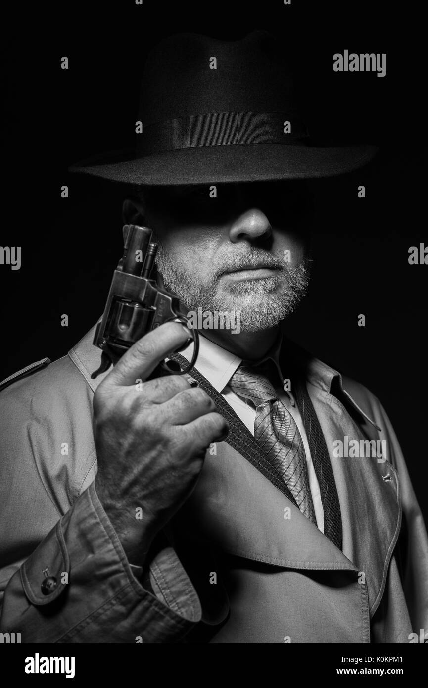 Detective tenant un pistolet dans le noir, il est vêtu d'un chapeau fedora et un trench coat, 1950 personnage film noir Banque D'Images