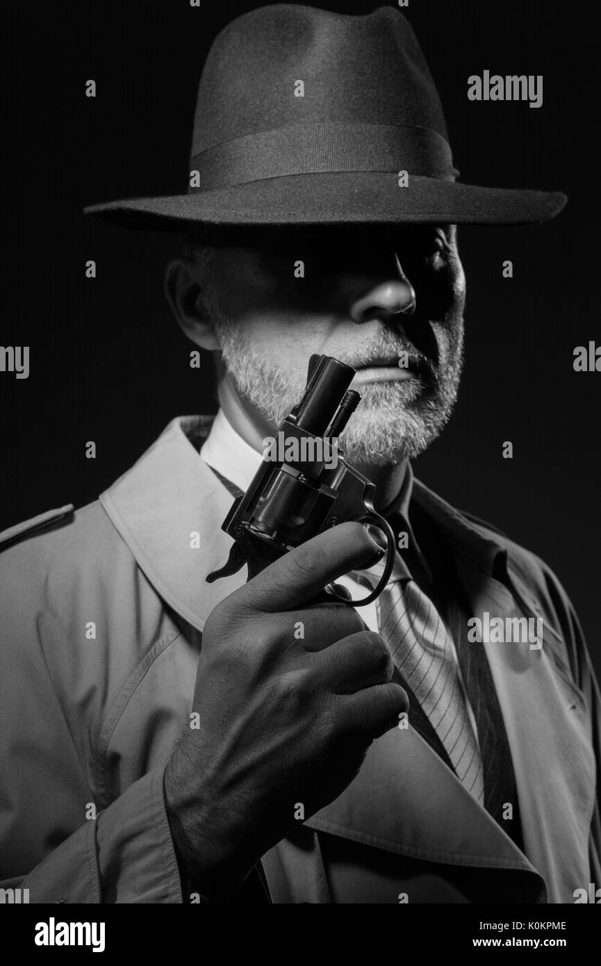 Style années 50 detective posant dans l'obscurité, il est tient une arme et portant un chapeau fedora, personnage de film noir Banque D'Images