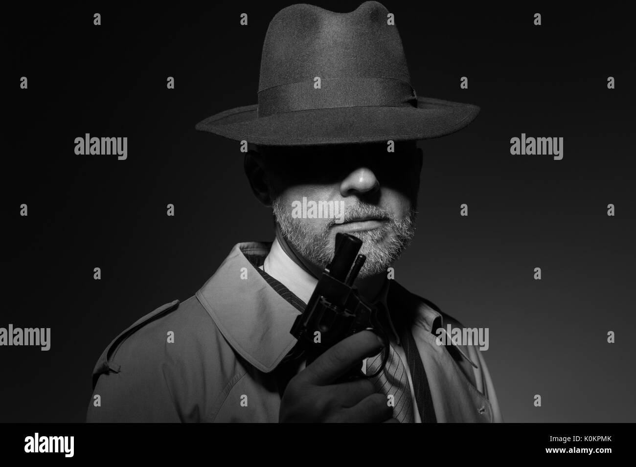 Detective tenant un pistolet dans le noir, il est vêtu d'un chapeau fedora et un trench coat, 1950 personnage film noir Banque D'Images