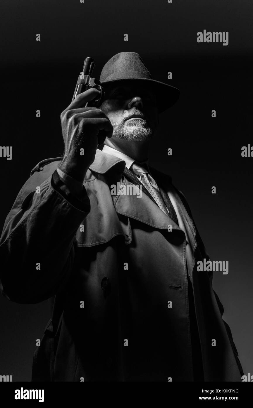 Style années 50 detective posant dans l'obscurité, il est tient une arme et portant un chapeau fedora, personnage de film noir Banque D'Images