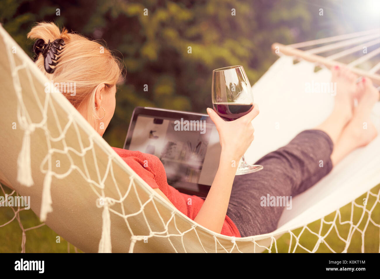 Belle femme de vous détendre sur un hamac avec verre de vin et la navigation sur le web sur une tablette (effet de génération). Banque D'Images