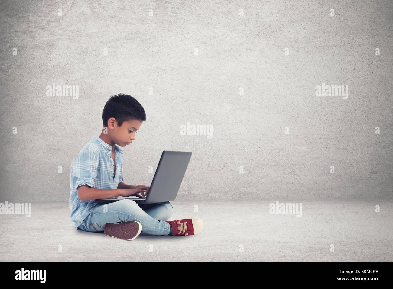 Heureux garçon assis à l'étage avec un ordinateur portable Banque D'Images