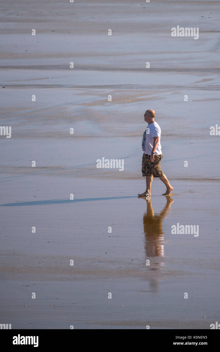 Un homme seul marche le long de la côte à marée basse. Banque D'Images