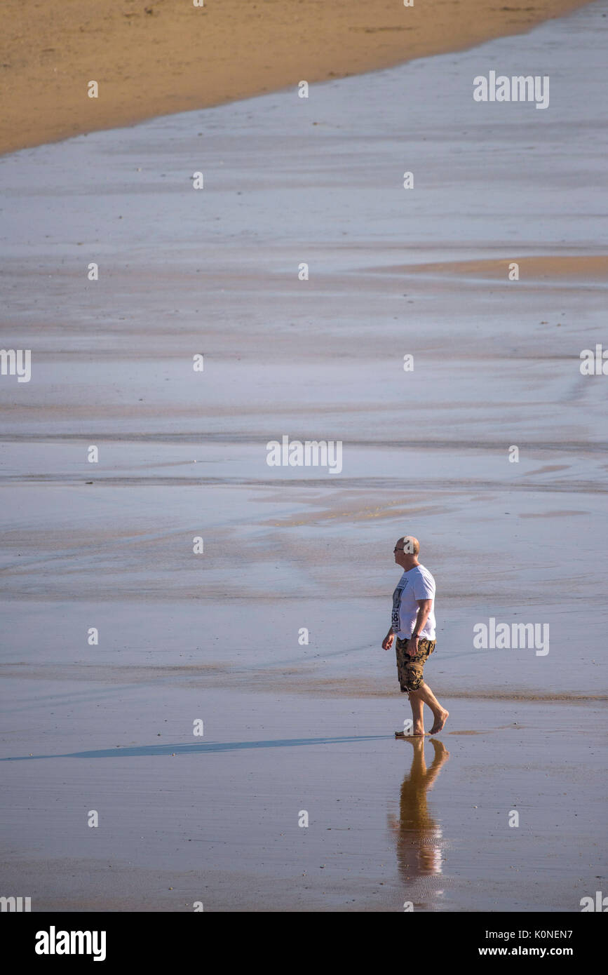 Un homme seul marche le long de la côte à marée basse. Banque D'Images