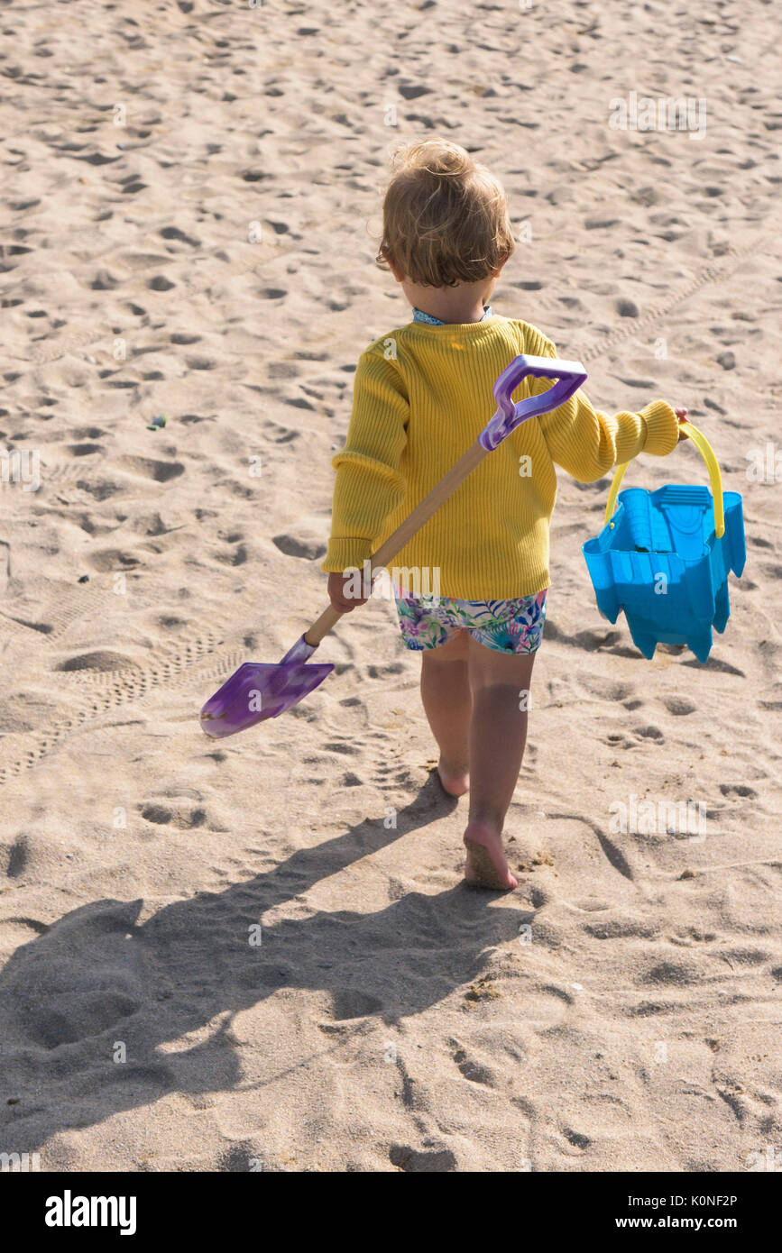 Un enfant en portant son seau et spade walking off pour jouer sur la plage. Banque D'Images