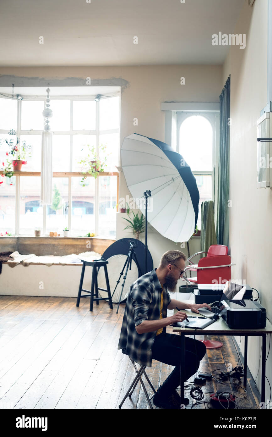 Vue de côté de l'aide photographe tablette graphique lors de l'édition à table en studio Banque D'Images