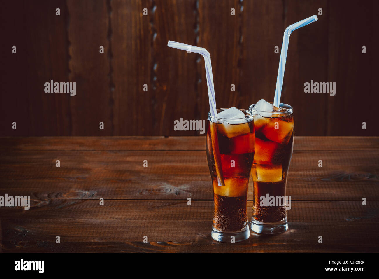 Beau verre de coca avec des glaçons avec une chaudière de pailles dans les verres sur fond de bois avec de l'espace libre Banque D'Images