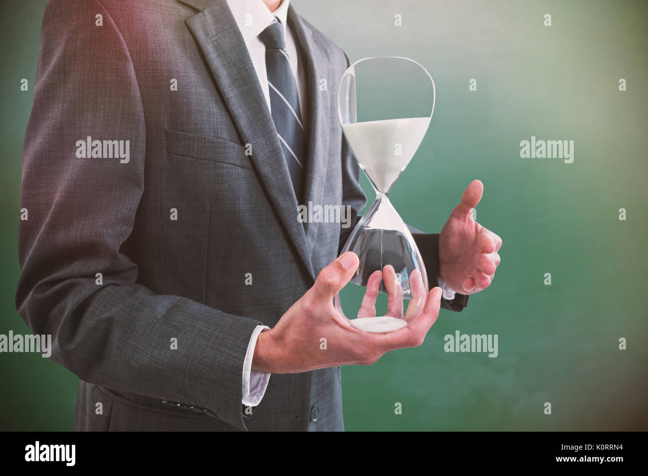 Mid section of businessman holding hourglass contre green chalkboard Banque D'Images Mid section of businessman holding hourglass contre green chalkboard Banque D'Images