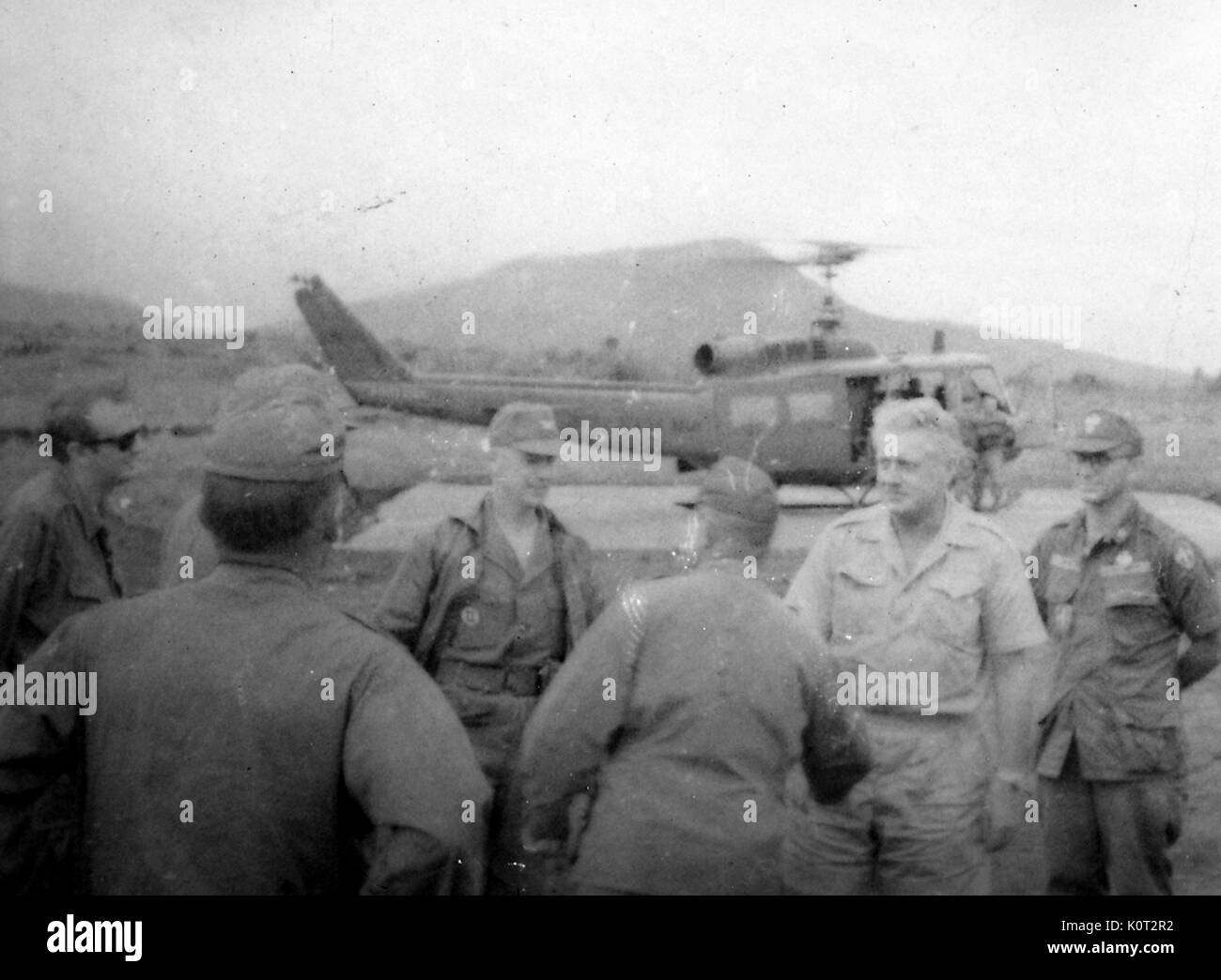 Soldats américains en uniforme militaire pendant la guerre du Vietnam debout dans un groupe, un hélicoptère Huey prépare à décoller d'une hélisurface en arrière-plan, 1966. Banque D'Images