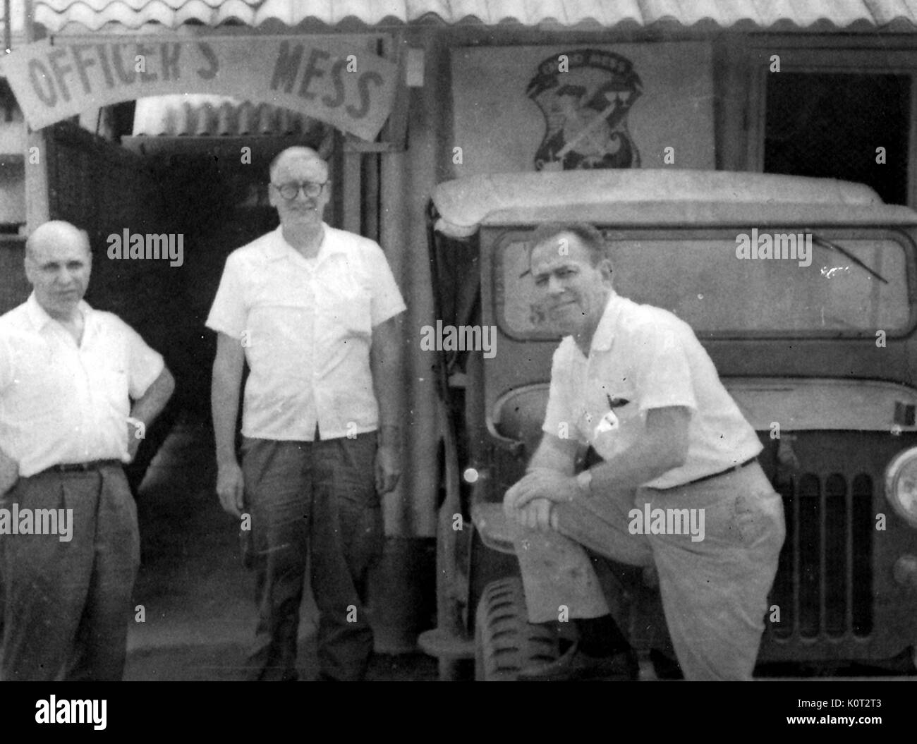 3 United States officiers militaires debout devant une salle du mess des officiers au Vietnam pendant la guerre du Vietnam, un officier avec son pied sur le pneu d'une Jeep, 1966. Banque D'Images