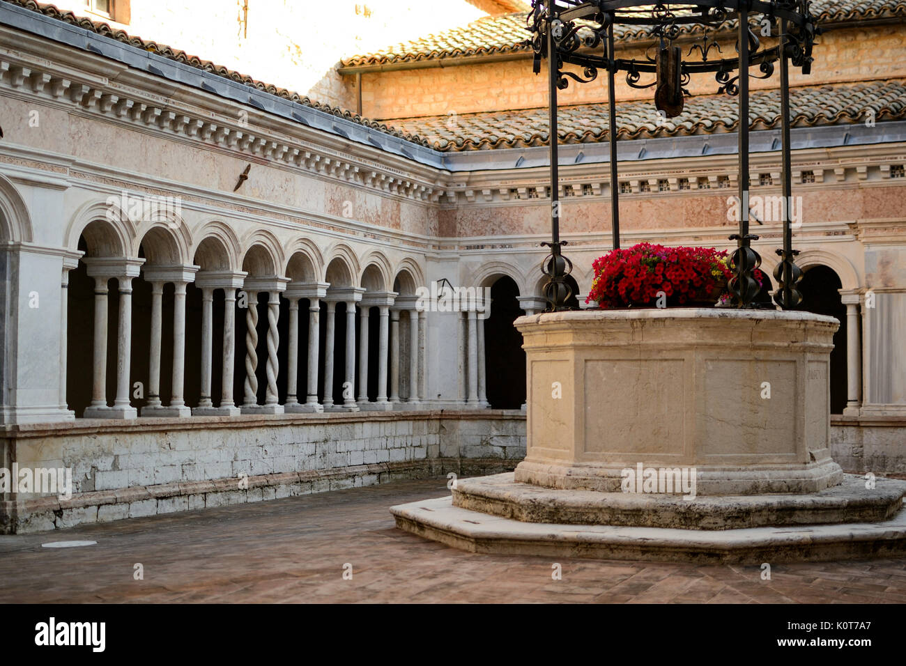 Ancien puits avec des fleurs dans un cloître de l'abbaye de Sassovivo (Italie). Le format paysage. Banque D'Images