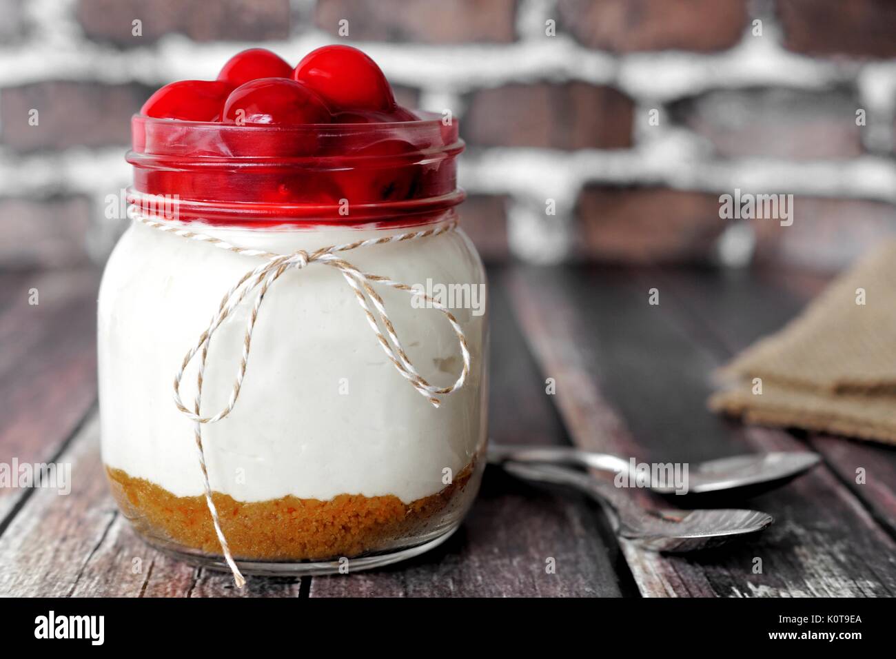 Délicieux gâteau cerise dans un pot Mason sur fond brique rustique avec du bois Banque D'Images Délicieux gâteau cerise dans un pot Mason sur fond brique rustique avec du bois Banque D'Images